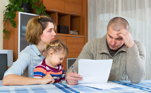 Photo of a family - a man, a woman and a child - looking at a bill with concerned faces.