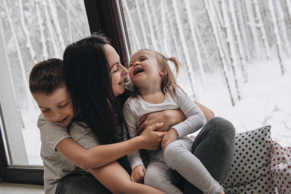 Family, mum and two children cuddling on a sofa with window behind them