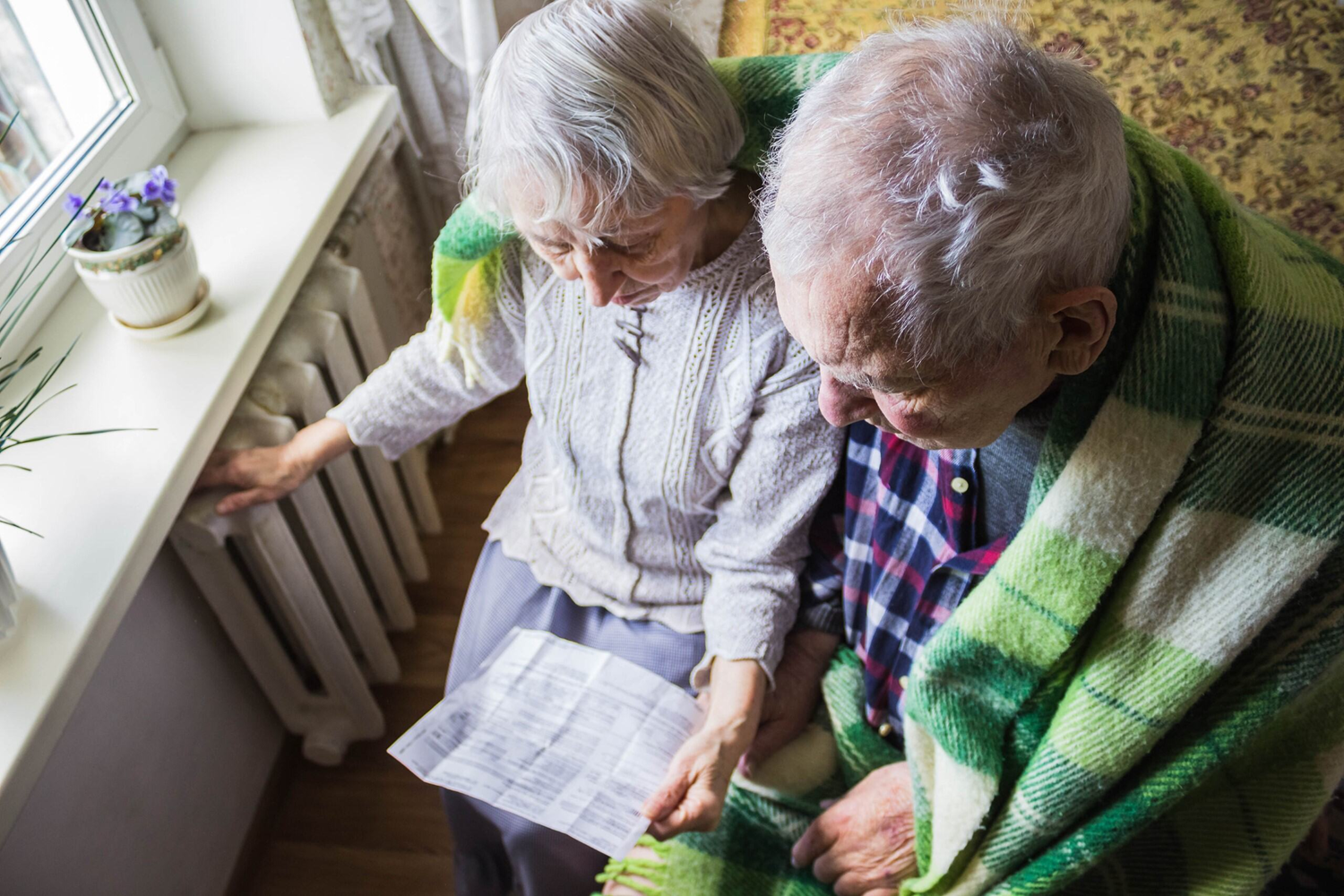An older couple wrapped in a blanket looks at an electricity bill.