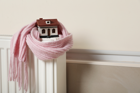 A wooden toy house wrapped in a pink scarf on a radiator.