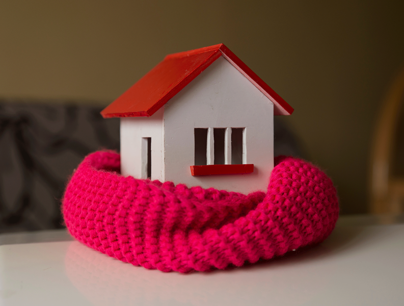 Red and white wooden toy house with a red scarf wrapped around it on a white table.