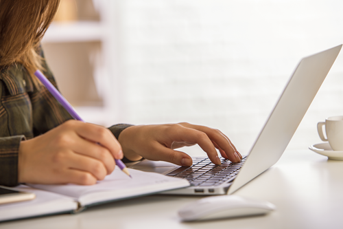 Woman checking data on her laptop and taking notes on a notebook.