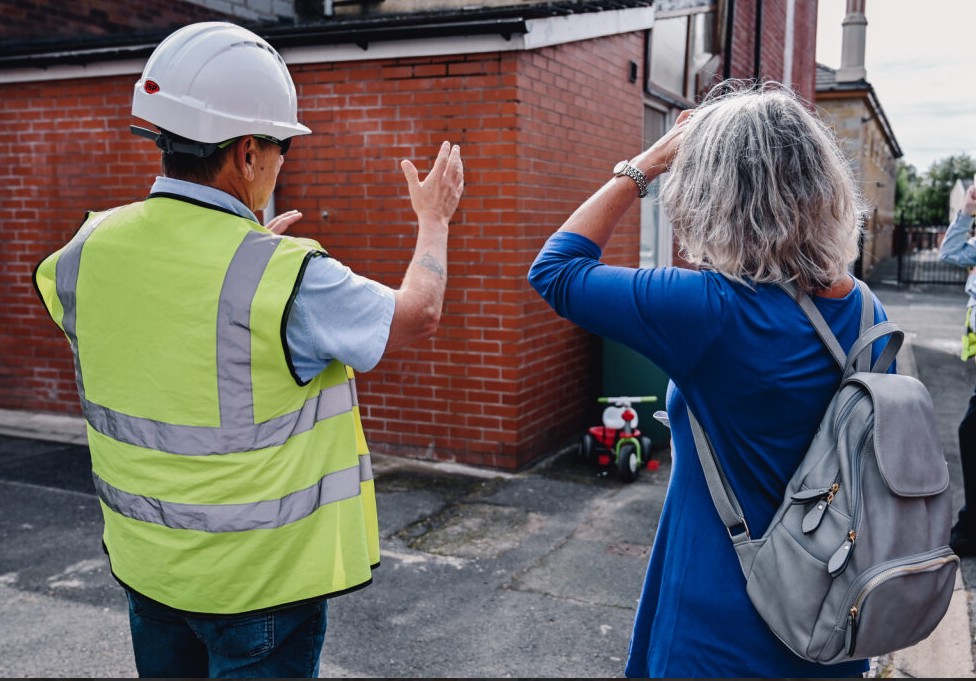 Contractor in high vis showing damp issues to a woman in Fishwick