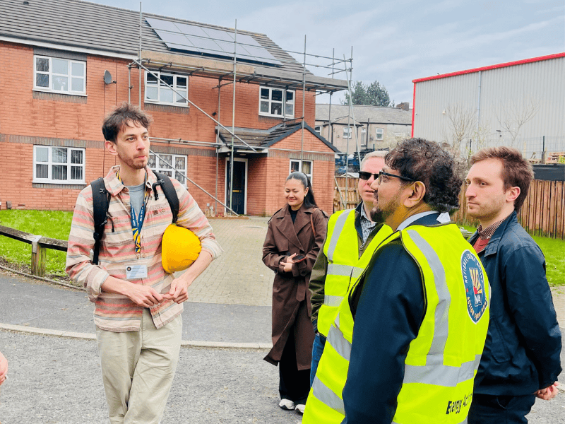 A member of our Retrofit Hub team talking to other people wearing high vis. Behind them is a house with solar panels.